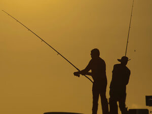 A silhouette of two men fishing with rods or poles.